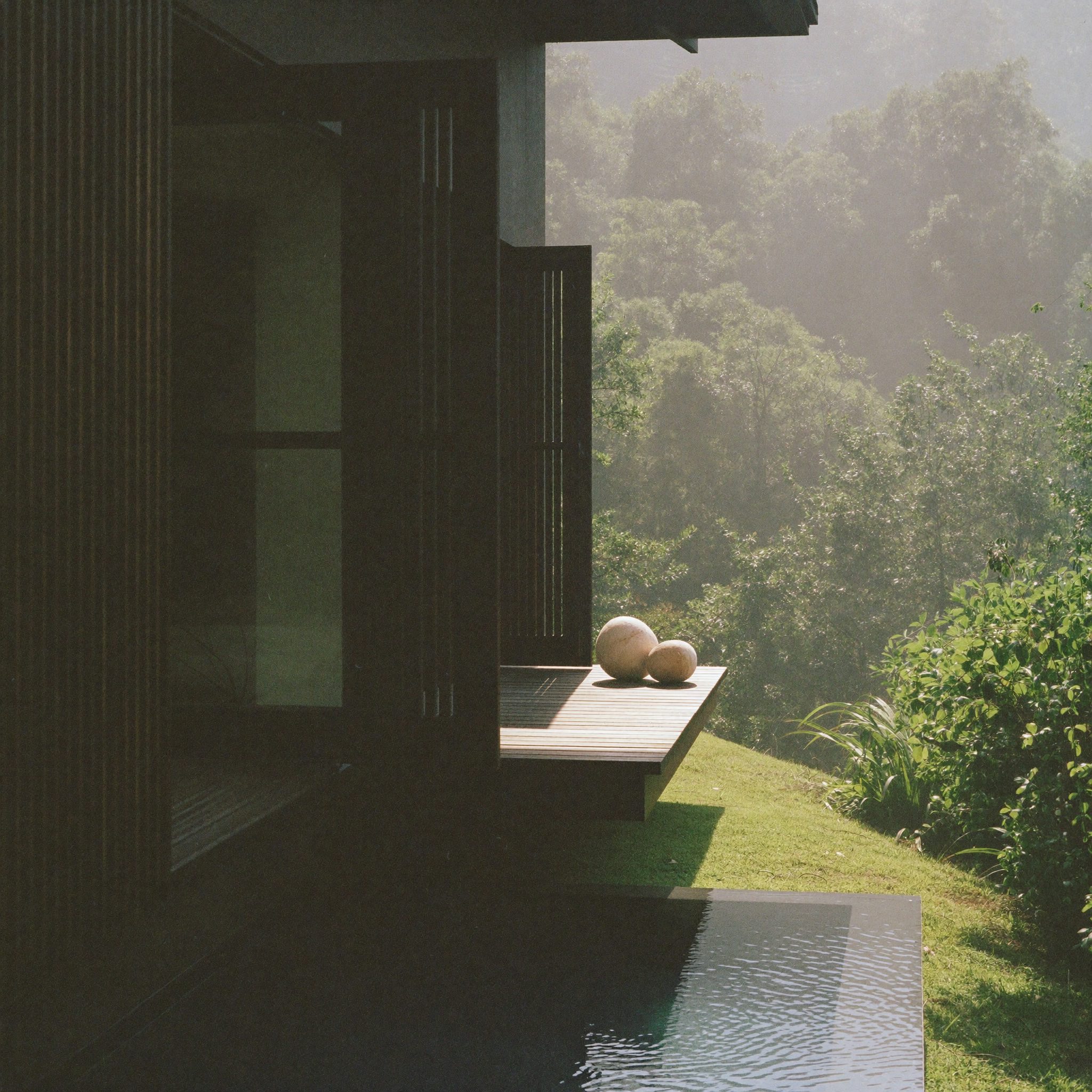 Rumah dengan teras kayu jati dan kolam di halaman tropis